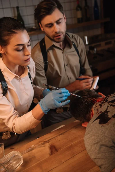 Cropped view of concentated female and male detectives collecting evidence from dead body and investigating crime scene — Stock Photo