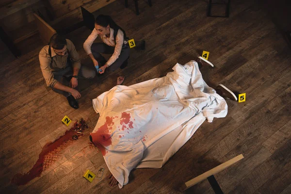 Детективы-женщины и мужчины расследуют мертвое тело, покрытое белым полотном на месте преступления — стоковое фото