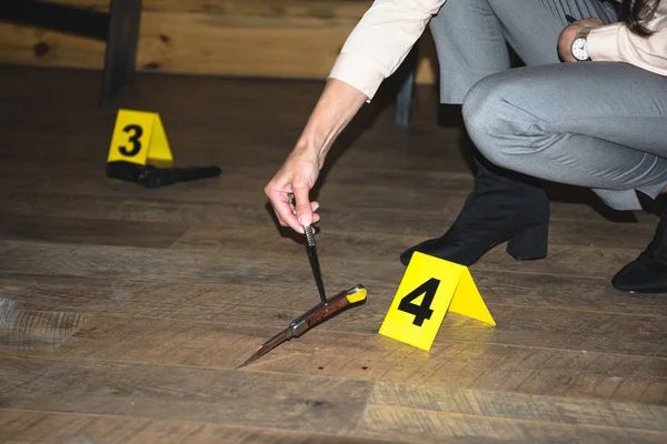 Cropped view of female hand examining knife near evidence markers at crime scene — Stock Photo
