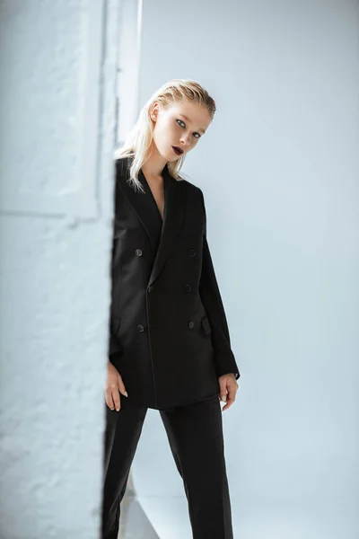 Beautiful blonde young woman in black suit posing on grey — Stock Photo