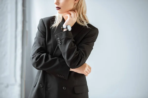 Ausgeschnittene Ansicht einer jungen Frau im schwarzen Anzug, die auf grau posiert — Stockfoto