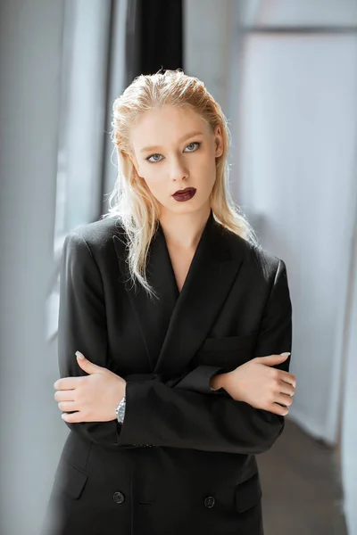 Elegante rubia joven en traje negro de moda posando en gris - foto de stock