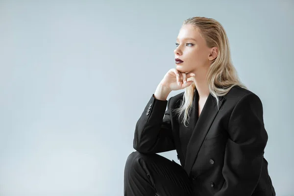 Attractive stylish girl posing in black suit for fashion shoot isolated on grey — Stock Photo
