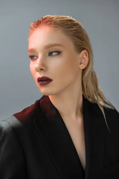 Atractiva mujer elegante posando en traje negro con luz roja aislada en gris - foto de stock