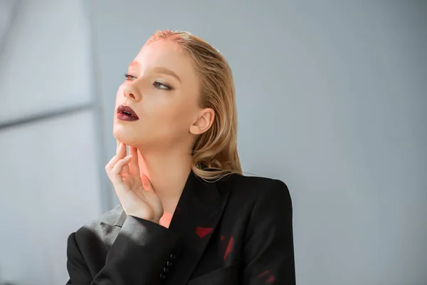 Fashionable blonde woman posing in black suit with red light on grey — Stock Photo