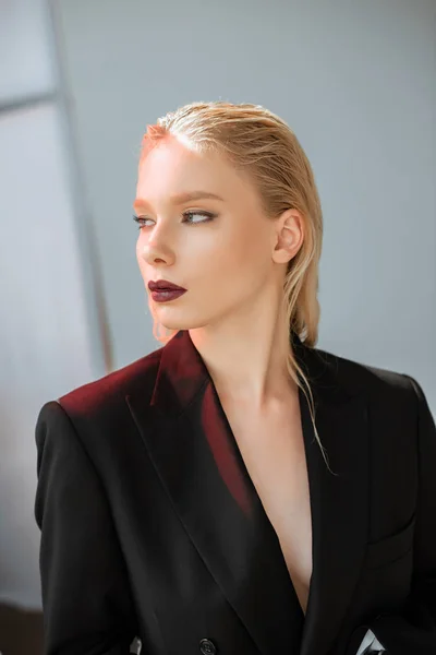 Jeune femme blonde à la mode posant en costume noir avec lumière rouge sur gris — Photo de stock