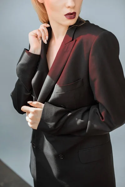 Cropped view of fashionable woman posing in black suit with red light on grey — Stock Photo