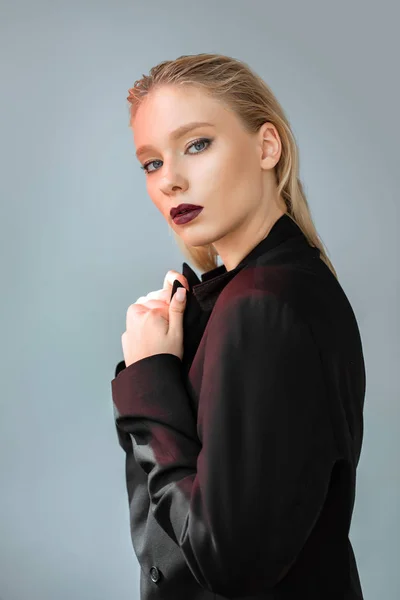 Belle femme posant en costume noir avec lumière rouge isolé sur gris — Photo de stock