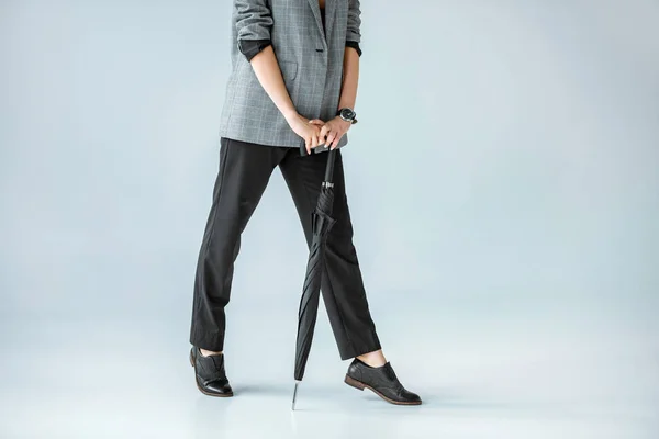 Vista recortada de la mujer de moda posando con paraguas en gris - foto de stock