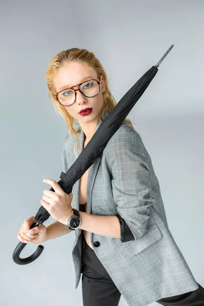 Attraktive blonde Mädchen mit Brille posiert mit Schirm isoliert auf grau — Stockfoto