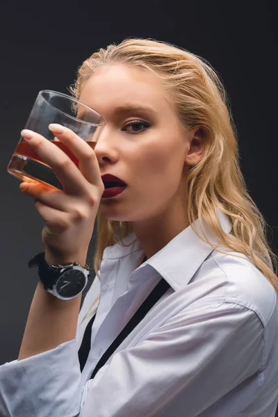 Beautiful elegant girl in formal wear holding glass of whiskey, isolated on dark grey — Stock Photo