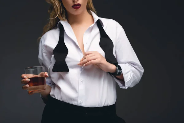 Vista ritagliata di ragazza alla moda in abbigliamento formale in possesso di vetro di cognac, isolato su grigio scuro — Foto stock