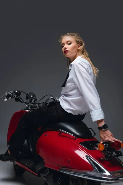 Hermosa chica de moda sentado en scooter rojo en gris - foto de stock