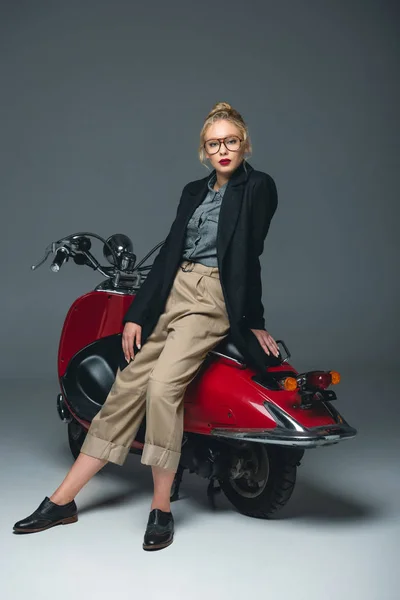 Модная элегантная девушка позирует на красном скутере на сером — стоковое фото