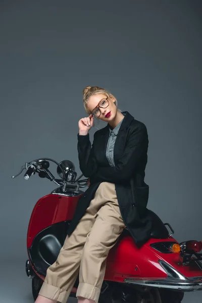 Beautiful fashionable girl posing on red scooter isolated on grey — Stock Photo