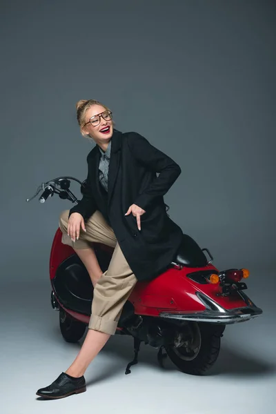 Fashionable laughing girl posing on red scooter on grey — Stock Photo