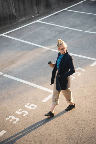 Bela menina elegante com café para ir andando no estacionamento — Fotografia de Stock