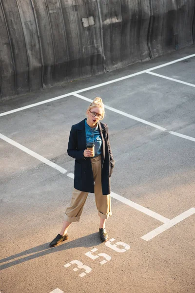 Elegante giovane donna con caffè per andare in posa sul parcheggio — Foto stock