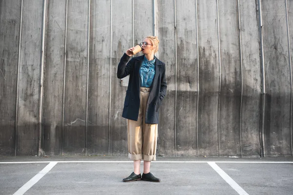 Fashionable girl drinking coffee to go on parking — Stock Photo