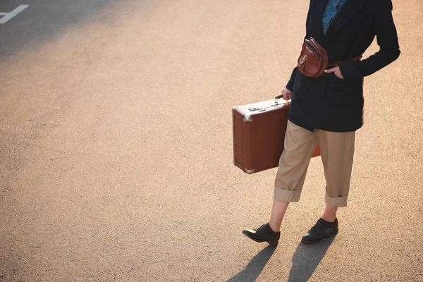 Vista sezione bassa della donna con borsa da viaggio retrò camminare su strada asfaltata — Foto stock