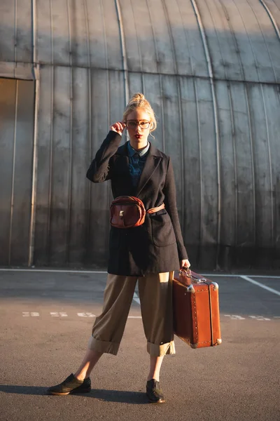 Belle voyageur à la mode tenant une valise rétro sur un parking urbain — Photo de stock