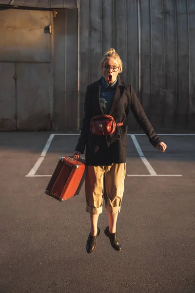 Stylish shocked girl jumping with vintage suitcase on urban parking — Stock Photo