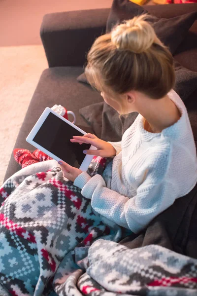 Angle view of young blonde woman sitting on couch and using tablet at home — Stock Photo