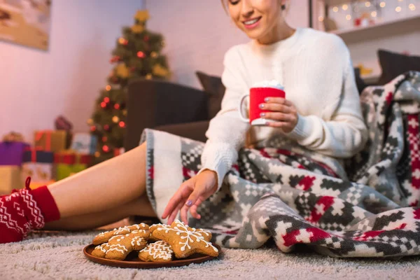 Woman in patterned blanked holding christmas gingerbread cookies and cocoa — Stock Photo