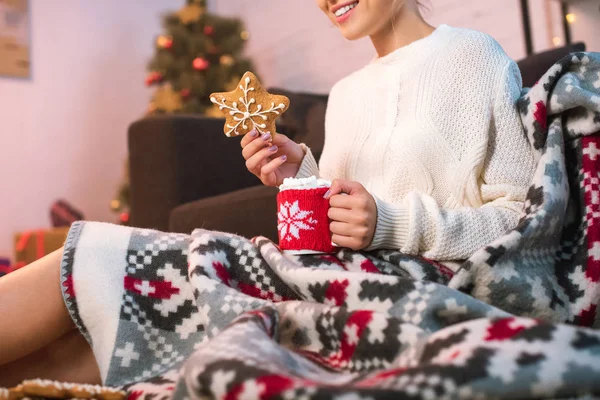 Woman in blanked holding christmas gingerbread cookie and cup with hot cocoa — Stock Photo