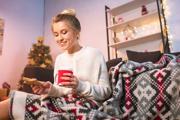 Woman in blanked holding christmas gingerbread cookie and cup with hot cocoa — Stock Photo