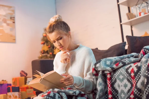 Thughtful woman reading book at home on Christmas eve — Stock Photo