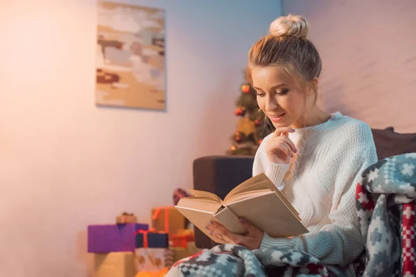 Charmante fille souriant et lecture livre à la maison le soir de Noël — Photo de stock