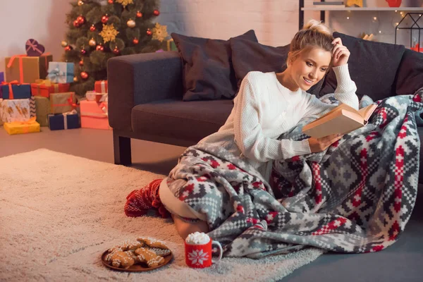 Чарівна дівчина посміхається і читає книгу вдома напередодні Різдва — стокове фото