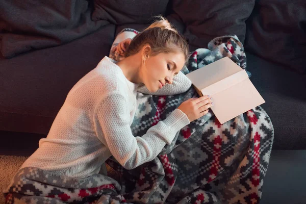 Schöne Frau mit Buch schlafend auf Sofa in gemusterter Decke — Stockfoto