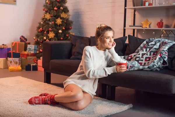 Веселая привлекательная женщина сидит на ковре с чашкой горячего какао — стоковое фото