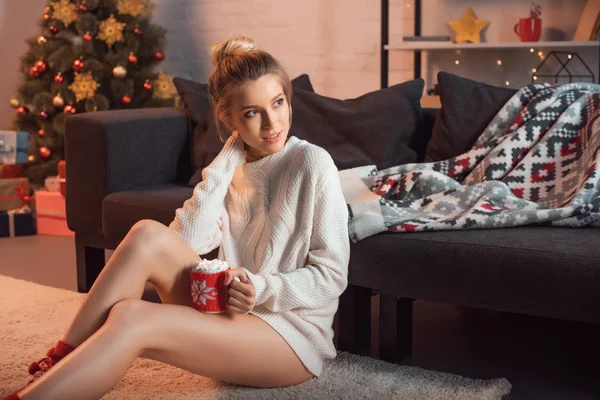 Beautiful woman sitting in christmas patterned socks on carpet with mug of cocoa — Stock Photo
