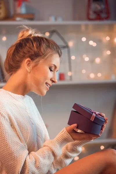 Sonriente joven rubia abriendo regalo en Navidad con fondo borroso - foto de stock