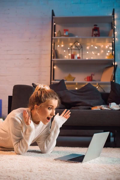 Aufgeregte junge blonde Frau liegt zur Weihnachtszeit mit Laptop am Boden — Stockfoto