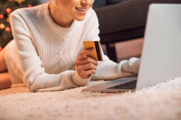 Ausgeschnittene Ansicht einer Frau, die auf dem Boden liegt, Kreditkarte in der Hand hält, Laptop benutzt und zu Weihnachten online einkauft — Stockfoto