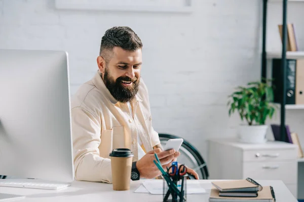 Lachender Geschäftsmann sitzt im Büro und schaut aufs Smartphone — Stockfoto