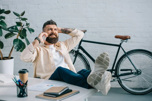 Erfolgreicher Geschäftsmann spricht auf Smartphone mit Beinen auf dem Schreibtisch — Stockfoto