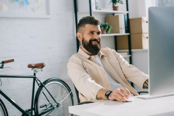 Hombre de negocios sonriente sentado en la oficina moderna y mirando al monitor - foto de stock