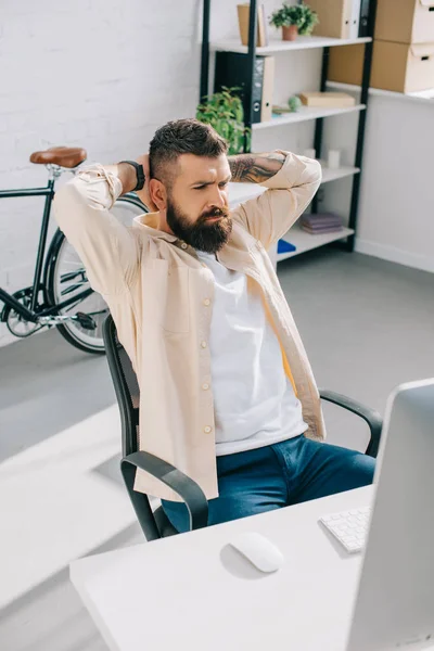 Bärtiger Geschäftsmann sitzt im Bürostuhl und legt die Hände hinter den Kopf — Stockfoto