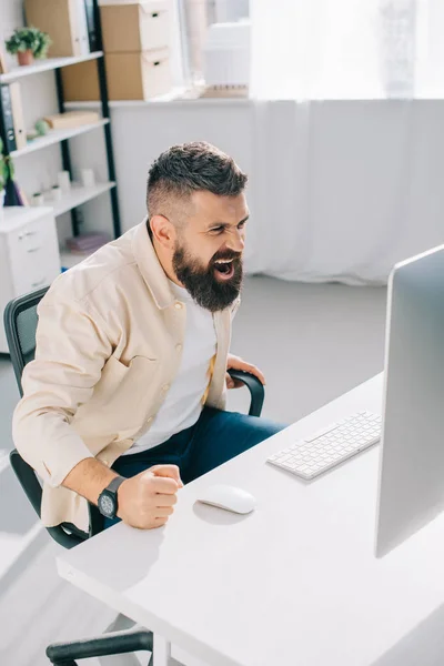 Impulsive businessman sitting in office chair, screaming and beating fist on desk — Stock Photo