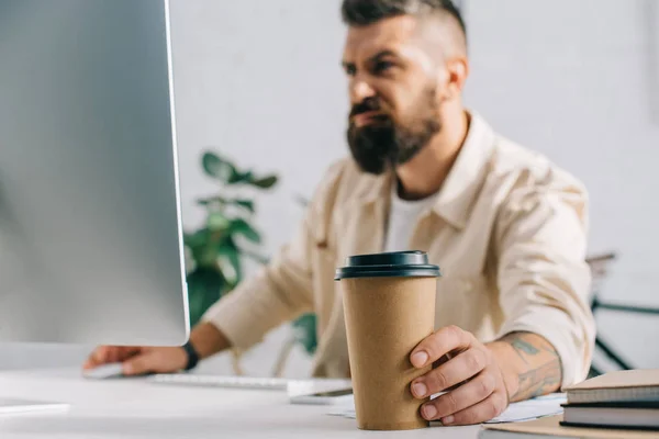 Homem irritado segurando xícara de café de papel e olhando para monitor de computador — Fotografia de Stock