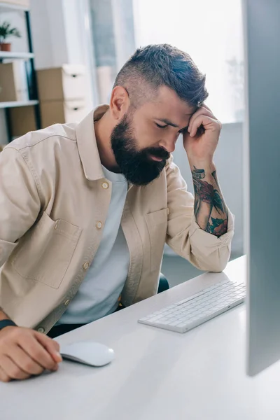 Homem de negócios desapontado sentado na mesa do computador e inclinado cabeça na mão no escritório — Fotografia de Stock