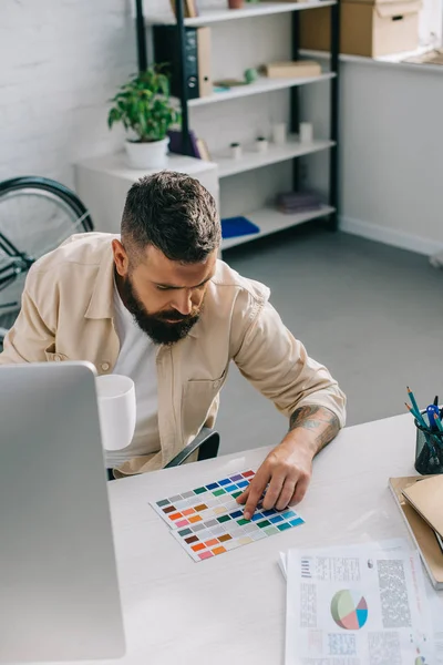 Designer masculin regardant à la palette de couleurs avec une tasse de thé au bureau — Photo de stock