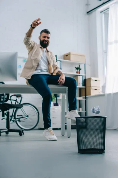Веселый человек бросает бумагу в мусорное ведро в современном офисе — стоковое фото