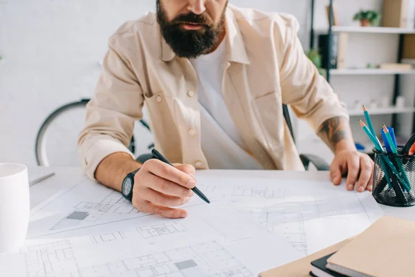 Bearded architect sitting at desk and working with blueprints — Stock Photo