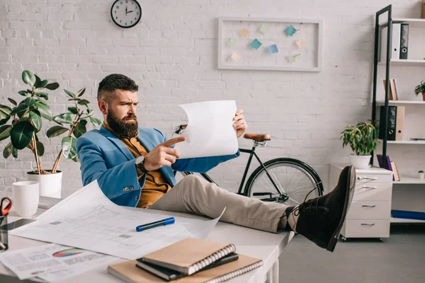 Männlicher Architekt sitzt am Schreibtisch und schaut im Büro auf Papier — Stockfoto